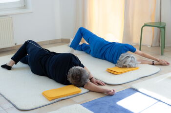 Zwei Frauen rollen am Boden auf die Rechte Seite, der rechte Arm ist gestreckt und sie rollen mit dem Kopf auf den rechten Arm.